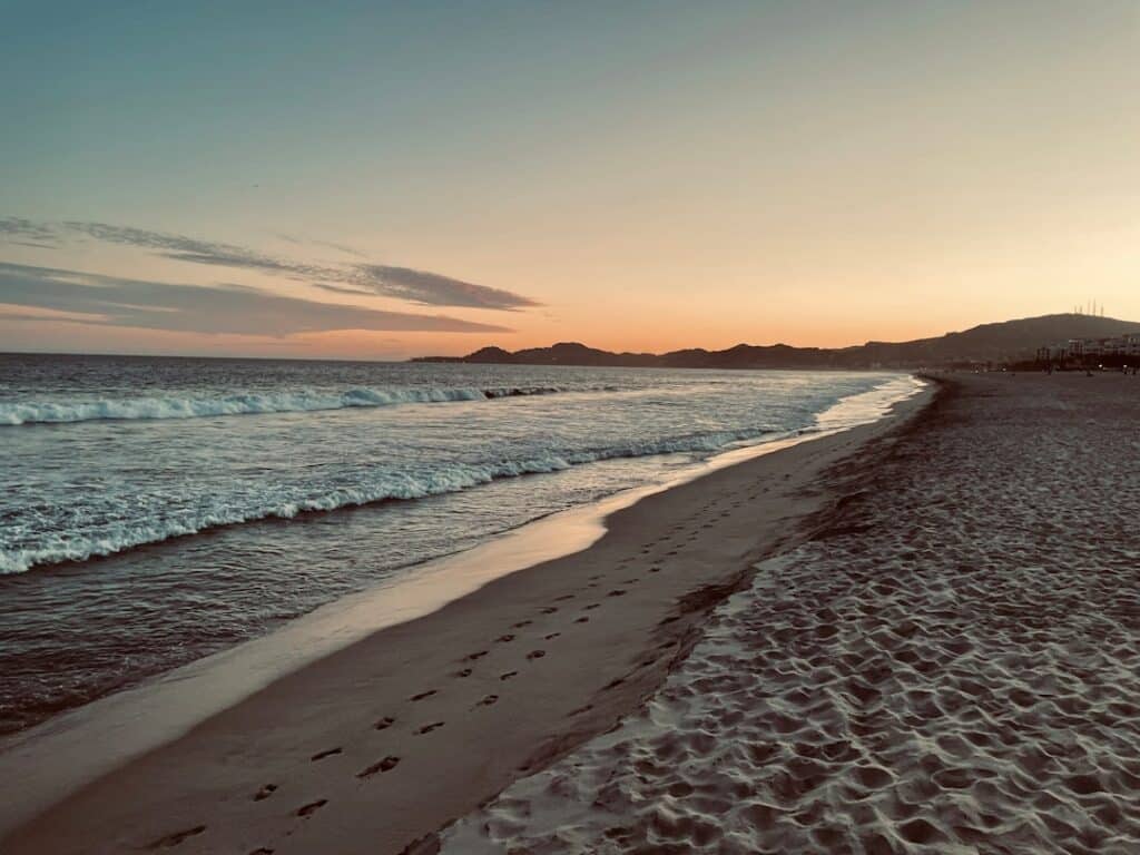 Woman practices a yoga pose on a tranquil beach in San José del Cabo as the sun rises over the ocean, creating a peaceful ...